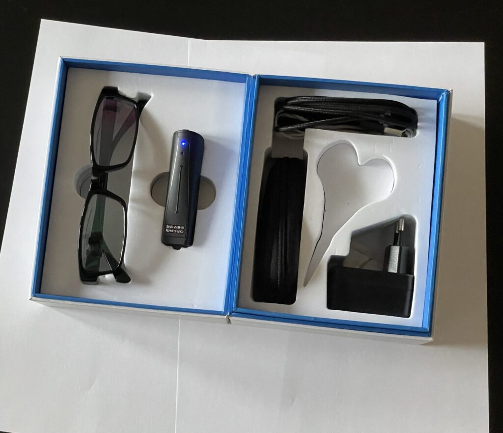 Otvorená krabica s OrCamom a príslušenstvom - okuliare, OrCam, puzdro, nabíjačka, kábel, šnúrka na krk